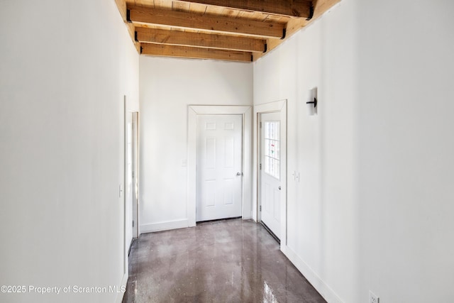 corridor with concrete flooring, baseboards, and beamed ceiling