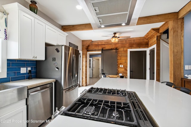 kitchen with white cabinets, beam ceiling, wood walls, ceiling fan, and appliances with stainless steel finishes