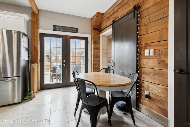 dining area featuring a barn door, wood walls, french doors, and light tile patterned floors