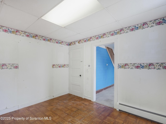 unfurnished room with baseboard heating, a paneled ceiling, and dark parquet floors