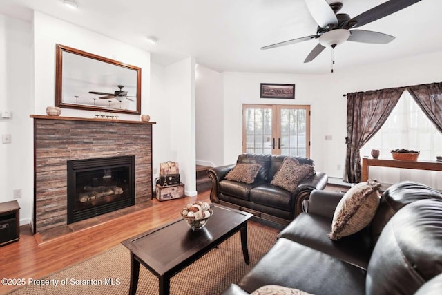 living room featuring a fireplace, wood-type flooring, a baseboard radiator, ceiling fan, and french doors