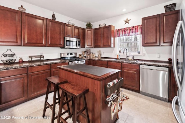 kitchen with sink, light tile patterned floors, appliances with stainless steel finishes, a kitchen island, and a kitchen bar