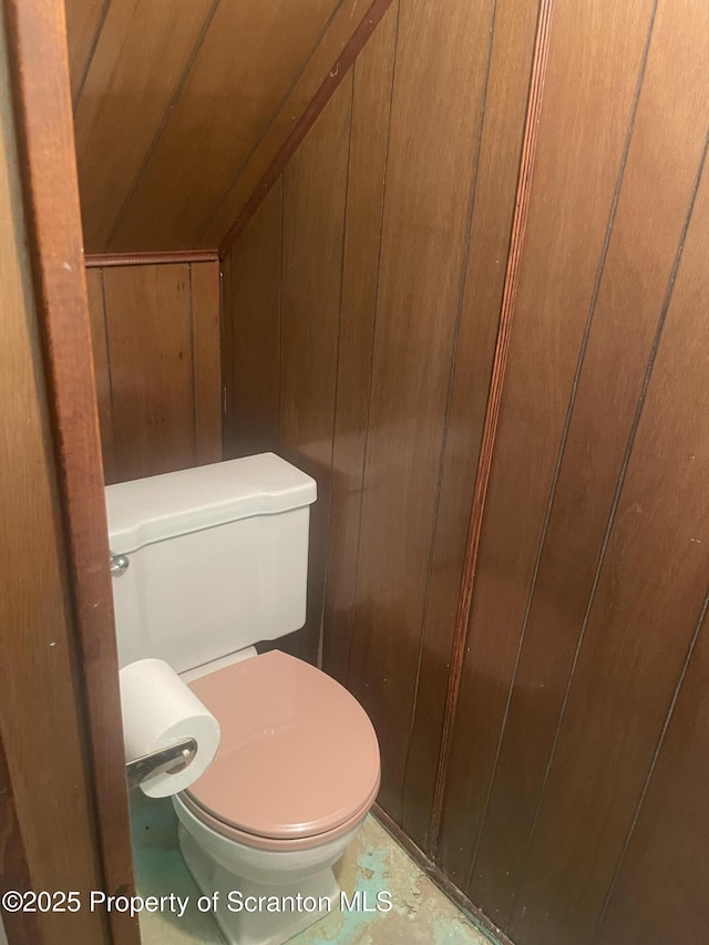 bathroom featuring lofted ceiling, toilet, and wooden walls