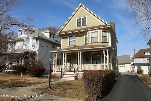 view of front of property with covered porch, a chimney, a detached garage, and an outbuilding