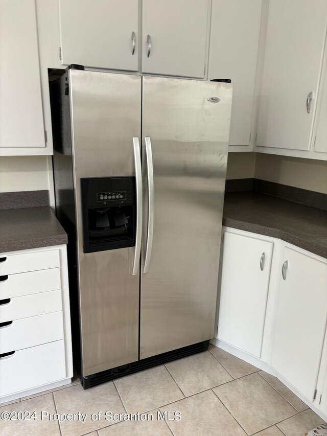 kitchen featuring stainless steel fridge, white cabinetry, light tile patterned flooring, and dark countertops