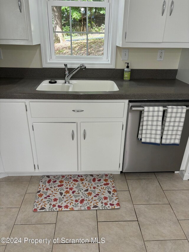 kitchen with stainless steel dishwasher, dark countertops, white cabinets, a sink, and light tile patterned floors