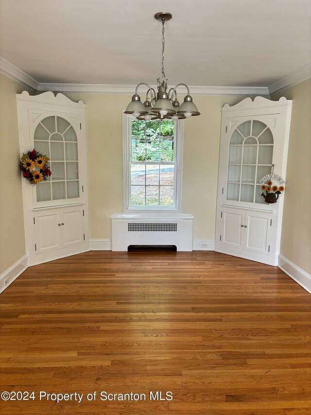 unfurnished dining area with an inviting chandelier, ornamental molding, wood finished floors, baseboards, and radiator heating unit
