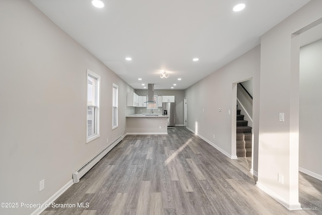 unfurnished living room featuring a baseboard heating unit, recessed lighting, light wood-style floors, and stairway