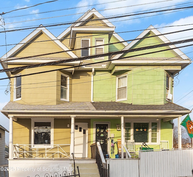 view of front facade featuring a porch, a shingled roof, and a fenced front yard