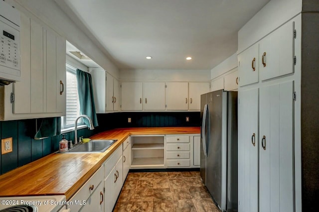 kitchen featuring white cabinets, wood counters, stainless steel fridge, and sink