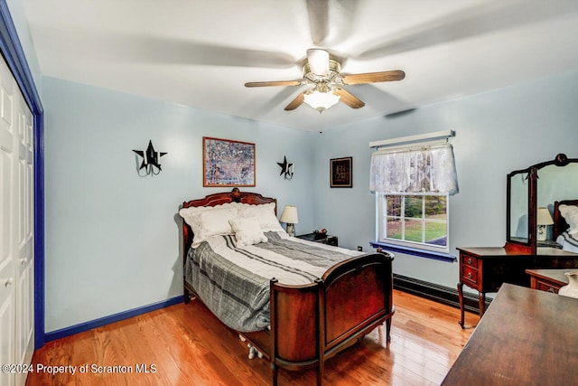 bedroom with hardwood / wood-style floors, ceiling fan, a baseboard heating unit, and a closet