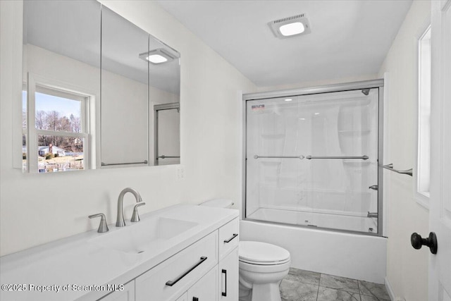 bathroom featuring toilet, vanity, combined bath / shower with glass door, and visible vents