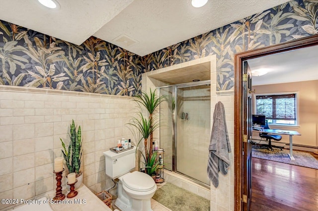 bathroom with a textured ceiling, a baseboard heating unit, an enclosed shower, and toilet