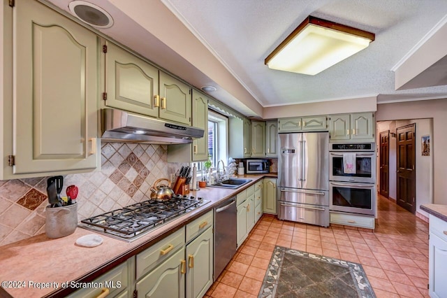 kitchen with tasteful backsplash, stainless steel appliances, crown molding, sink, and green cabinetry