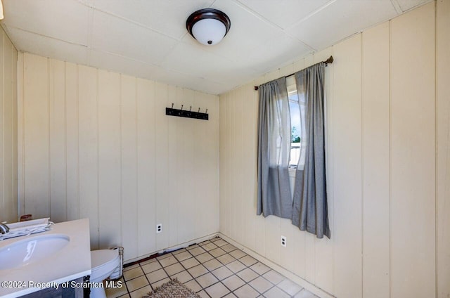 empty room with light tile patterned floors, sink, and wooden walls