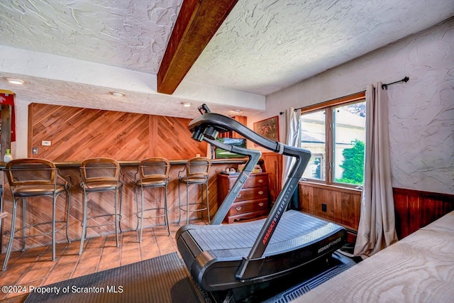 exercise room with tile patterned floors, bar, wooden walls, and a textured ceiling