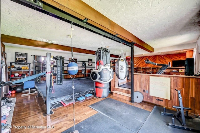 workout room with wood-type flooring, a textured ceiling, and wood walls