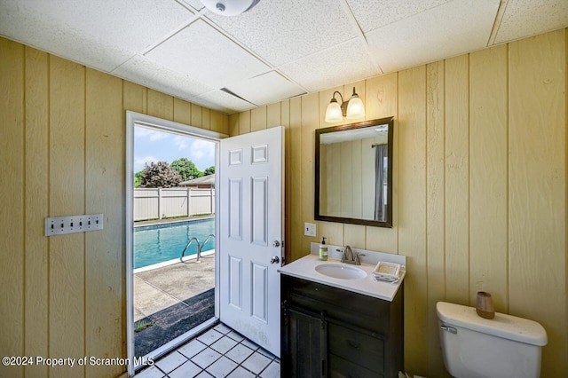 bathroom with a paneled ceiling, vanity, tile patterned floors, wooden walls, and toilet