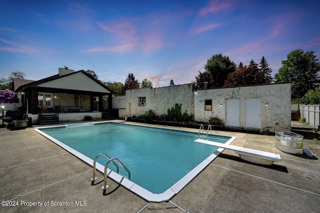 pool at dusk featuring a patio area and a diving board