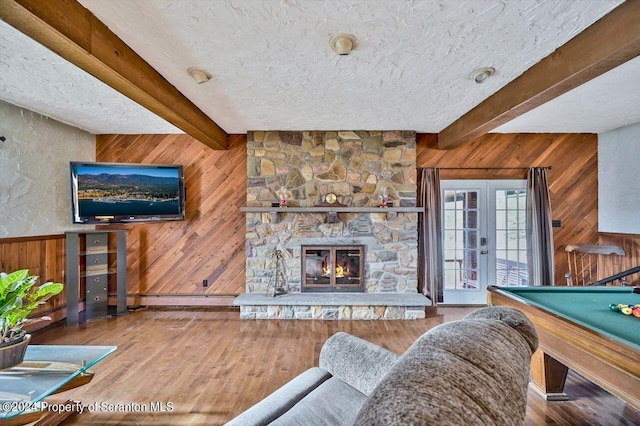 living room with french doors, a fireplace, wooden walls, beamed ceiling, and hardwood / wood-style floors