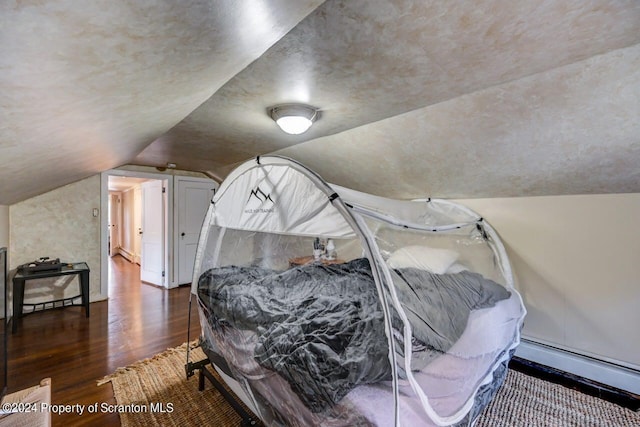 bedroom with dark hardwood / wood-style floors, lofted ceiling, and a baseboard heating unit