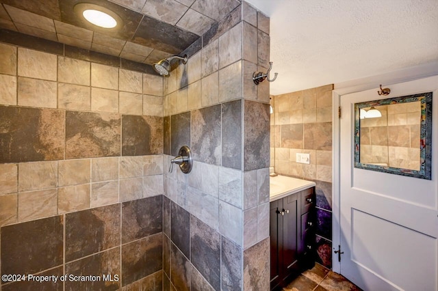 bathroom featuring a tile shower, vanity, a textured ceiling, and tile walls