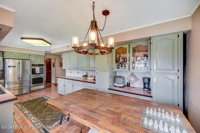 kitchen with pendant lighting, backsplash, green cabinets, a notable chandelier, and stainless steel appliances