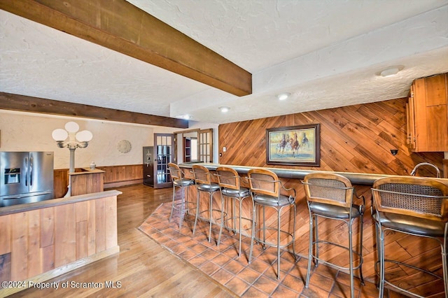 interior space featuring a kitchen bar, stainless steel fridge, a baseboard radiator, beamed ceiling, and wood walls