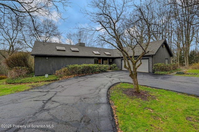 view of front facade featuring driveway, a chimney, and a garage