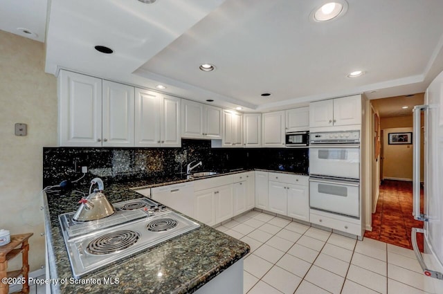 kitchen with white cabinets, stainless steel appliances, backsplash, light tile patterned floors, and a sink