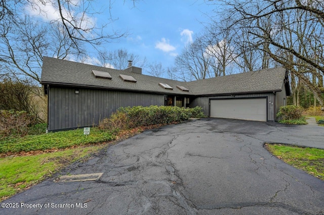 view of front facade featuring an attached garage, a chimney, driveway, and roof with shingles