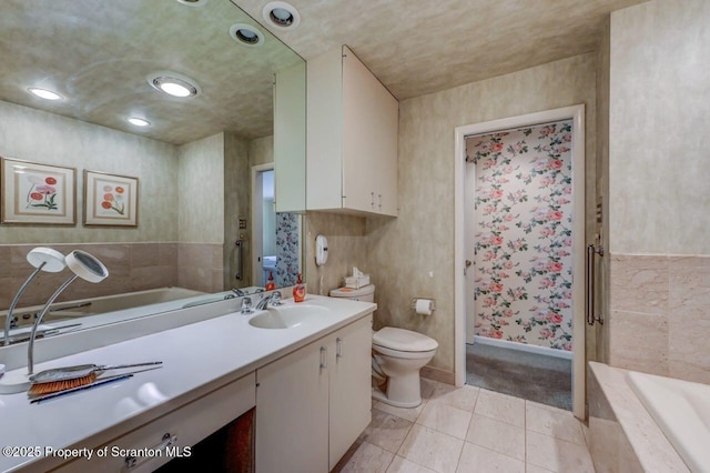 bathroom featuring tile patterned floors, toilet, baseboards, tiled bath, and vanity