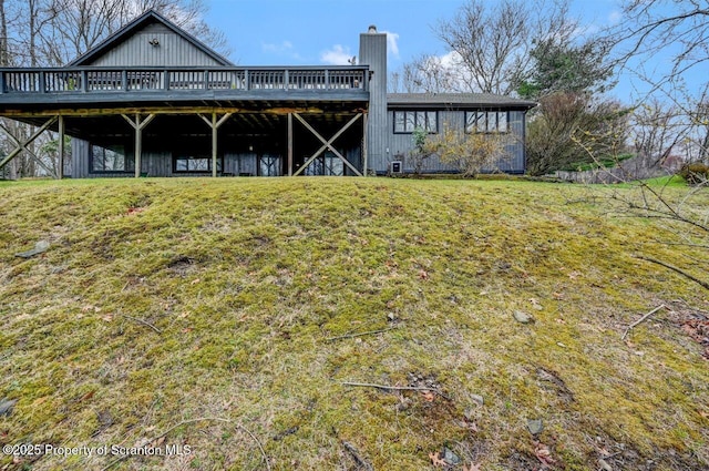 back of property featuring a chimney, a deck, and a lawn