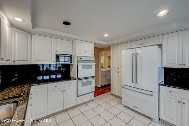 kitchen with dark stone counters, white appliances, light tile patterned floors, backsplash, and white cabinetry