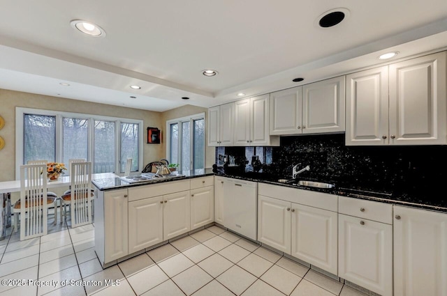 kitchen with white dishwasher, backsplash, light tile patterned flooring, and a peninsula