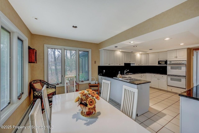 kitchen with a peninsula, a sink, tasteful backsplash, white cabinetry, and white double oven