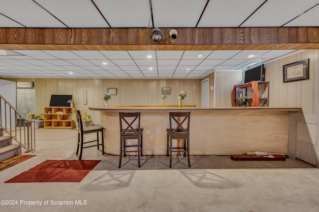 kitchen featuring light carpet, wooden walls, and a breakfast bar area