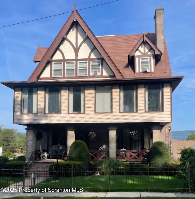 tudor home with covered porch, a fenced front yard, and a chimney