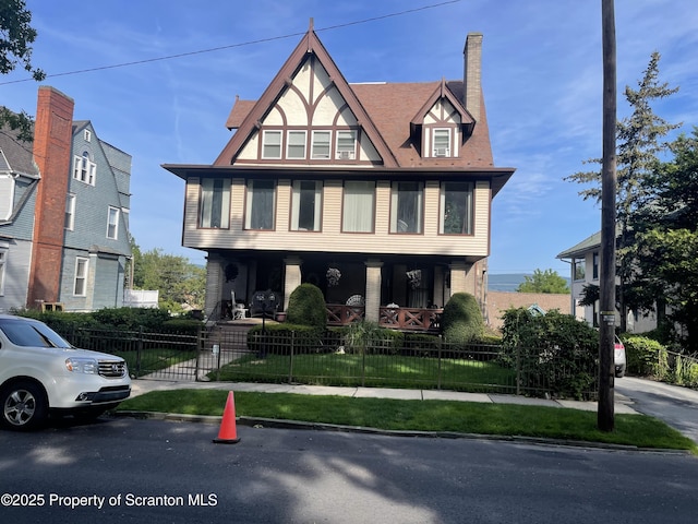 tudor home with a porch, a fenced front yard, and a chimney
