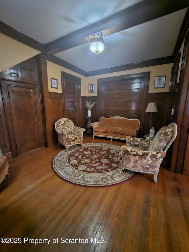 living room featuring beamed ceiling, wood walls, a wainscoted wall, and hardwood / wood-style floors