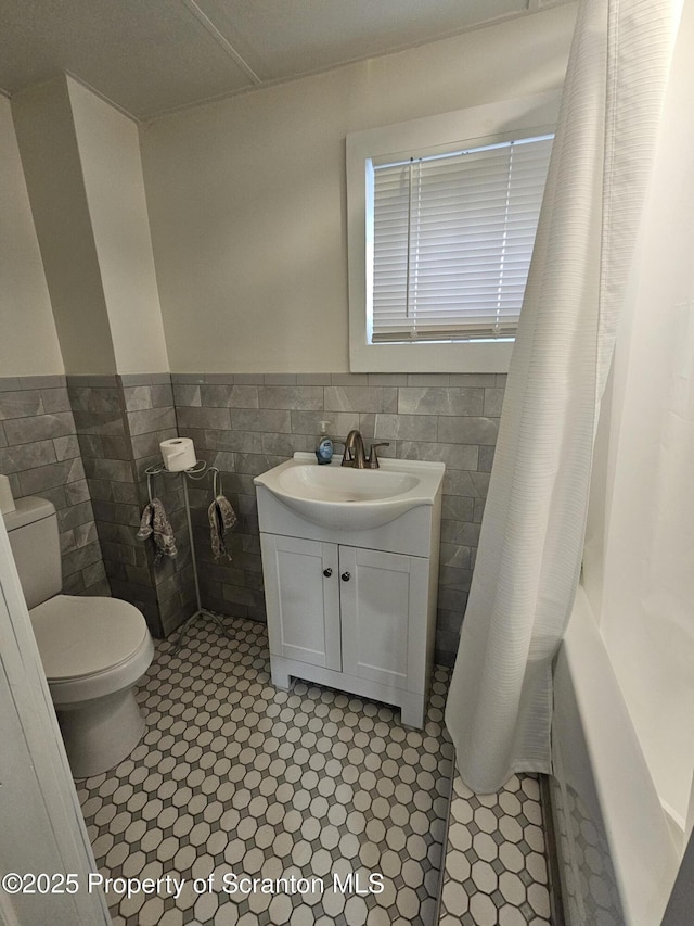 full bathroom featuring wainscoting, vanity, toilet, tile walls, and a shower with curtain