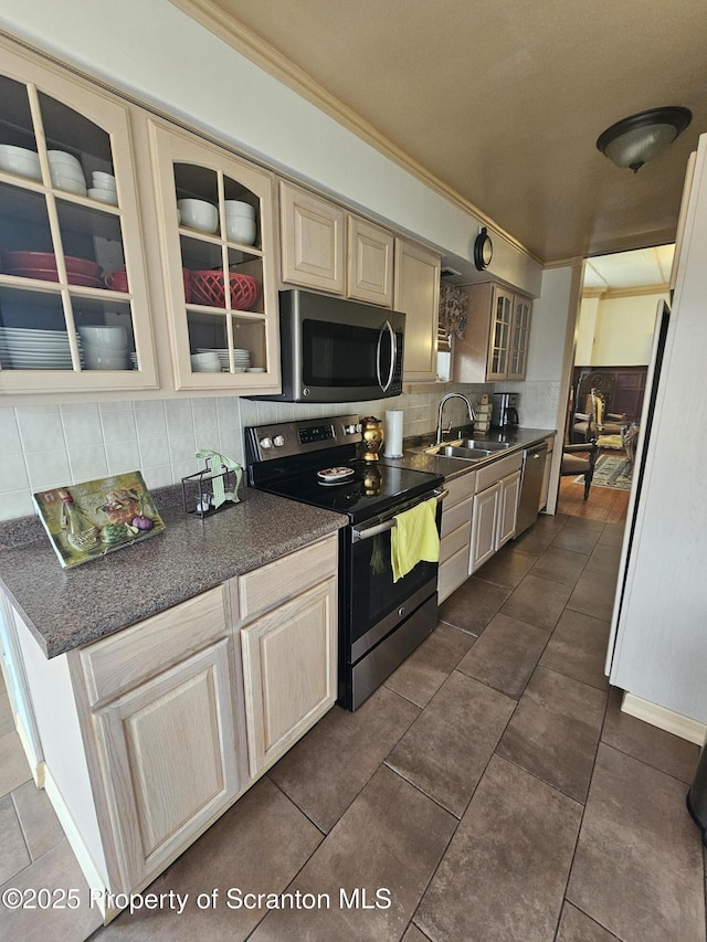 kitchen featuring dark countertops, appliances with stainless steel finishes, a sink, backsplash, and glass insert cabinets