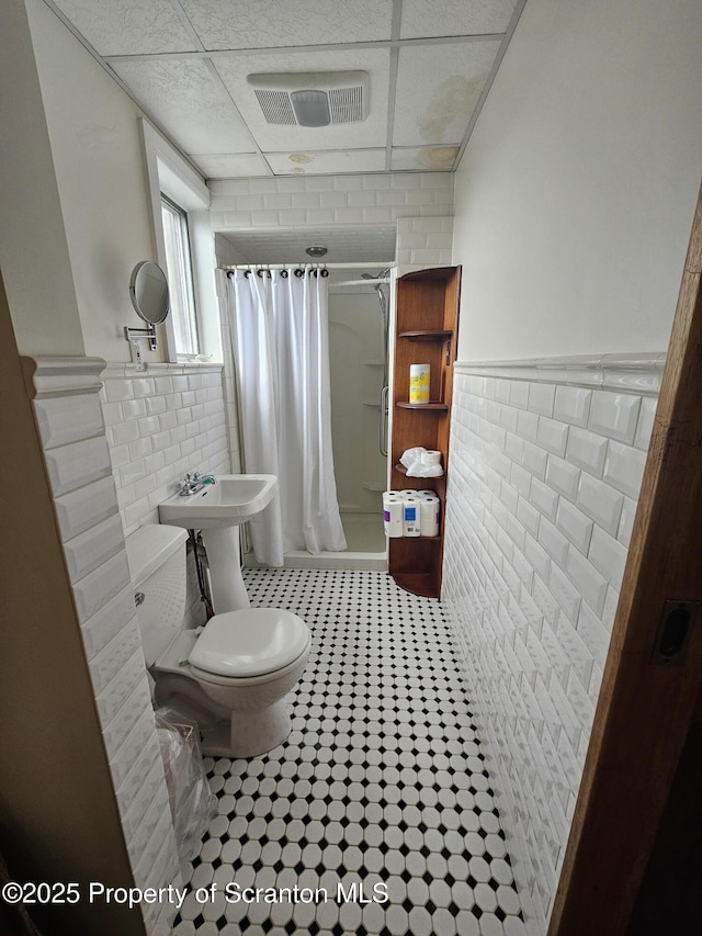 bathroom featuring visible vents, toilet, tile walls, a shower with shower curtain, and a drop ceiling