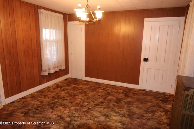 carpeted spare room featuring an inviting chandelier, radiator heating unit, and wooden walls