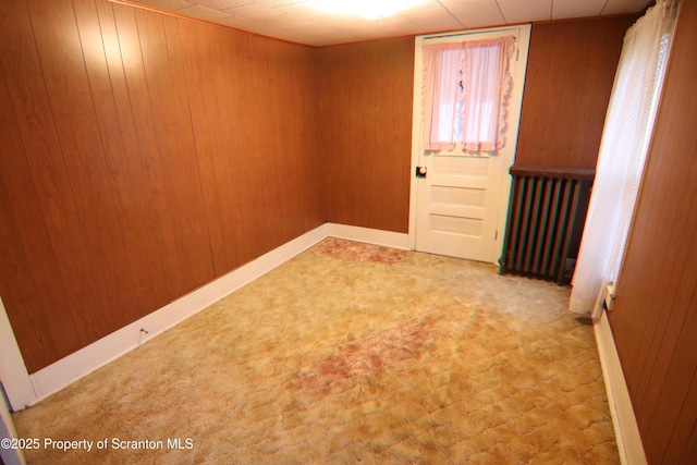 carpeted spare room featuring radiator heating unit and wood walls