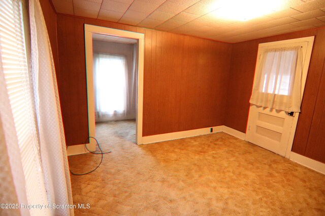 carpeted spare room featuring wood walls