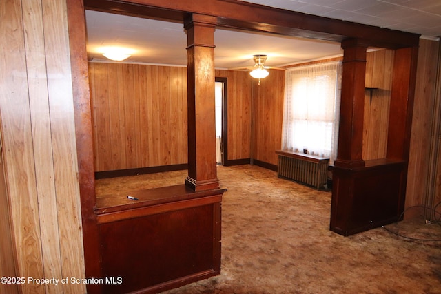 interior space featuring radiator heating unit, carpet floors, decorative columns, and wooden walls