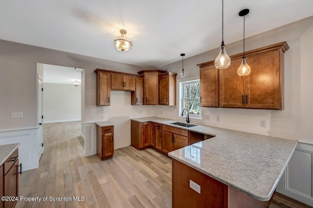 kitchen featuring kitchen peninsula, light wood-type flooring, sink, and hanging light fixtures