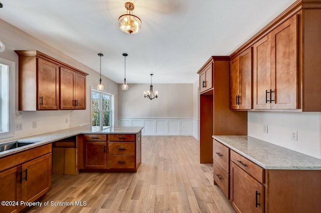 kitchen featuring decorative light fixtures, a notable chandelier, light wood finished floors, brown cabinetry, and a peninsula