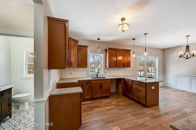 kitchen featuring sink, light hardwood / wood-style flooring, a notable chandelier, kitchen peninsula, and pendant lighting